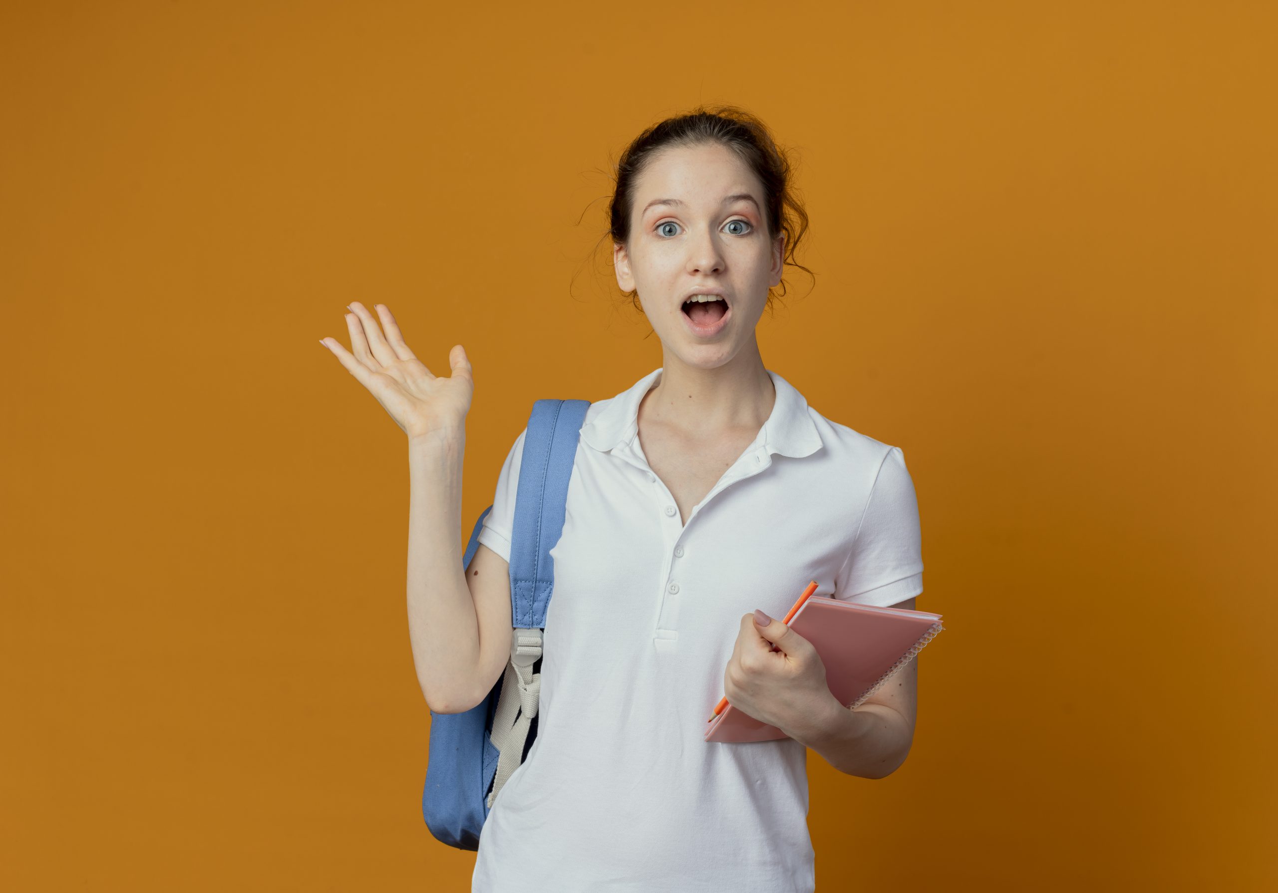 impressed young pretty female student wearing back bag holding note pad and pen showing empty hand isolated on orange background with copy space impressed young pretty female student wearing back bag holding note pad and pen showing empty hand isolated on orange background with copy space
